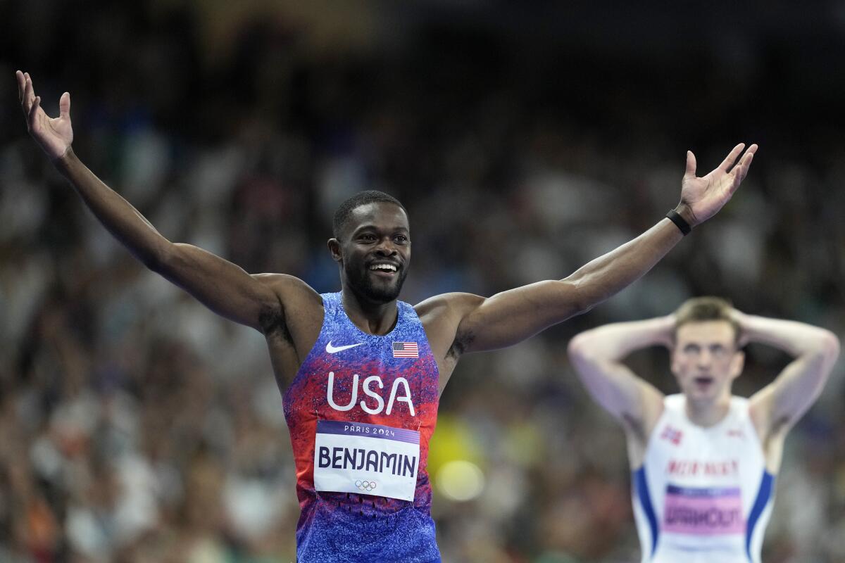 American Rai Benjamin holds up and out his arms while a competitor holds his head with his hands nearby.