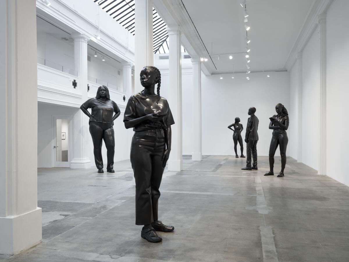 Large-scale bronzes show Black people engaged in quotidian activities (such as looking at their phone) inside a gallery