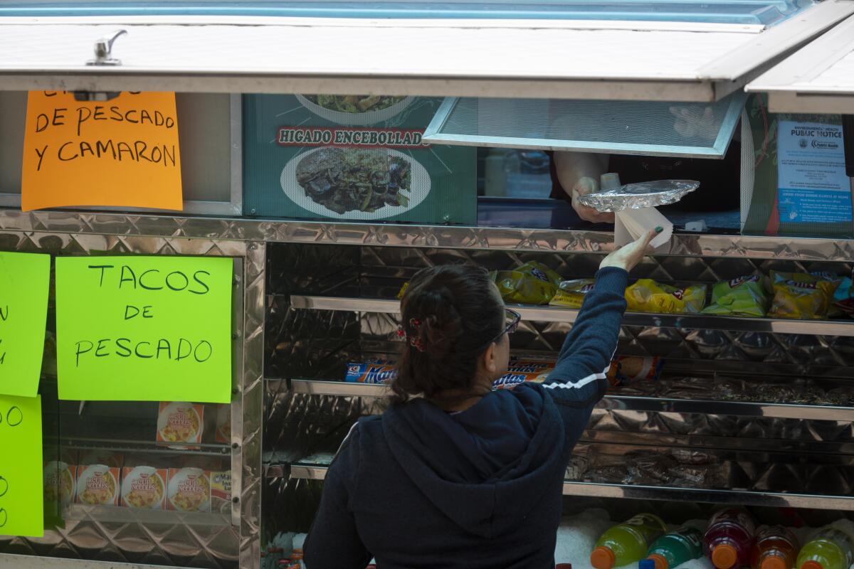 A woman is handed a meal from a food truck employee.