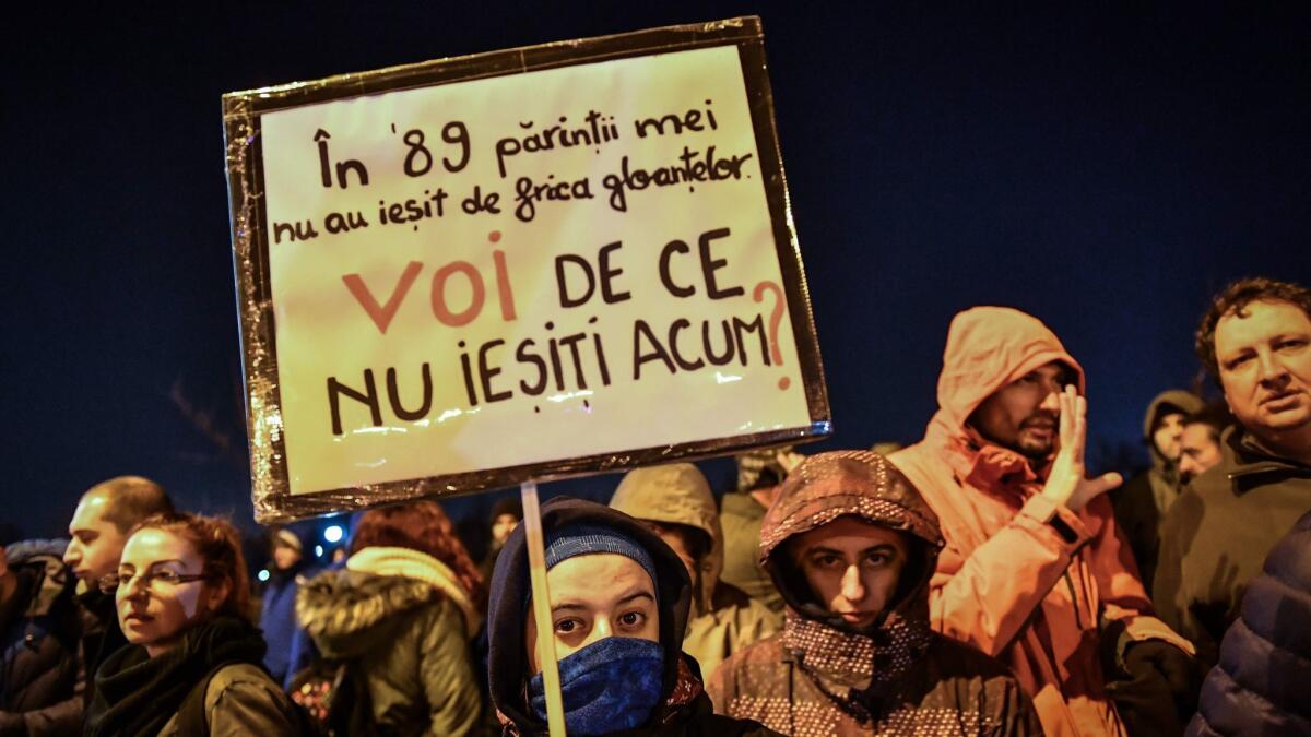 A woman holds a placard reading "In '89, my parents feared the bullets and didn't go out (to protest) / What is YOUR excuse today, not to go out?" during a protest next to the Parliament in Bucharest on Dec. 21, 2017.