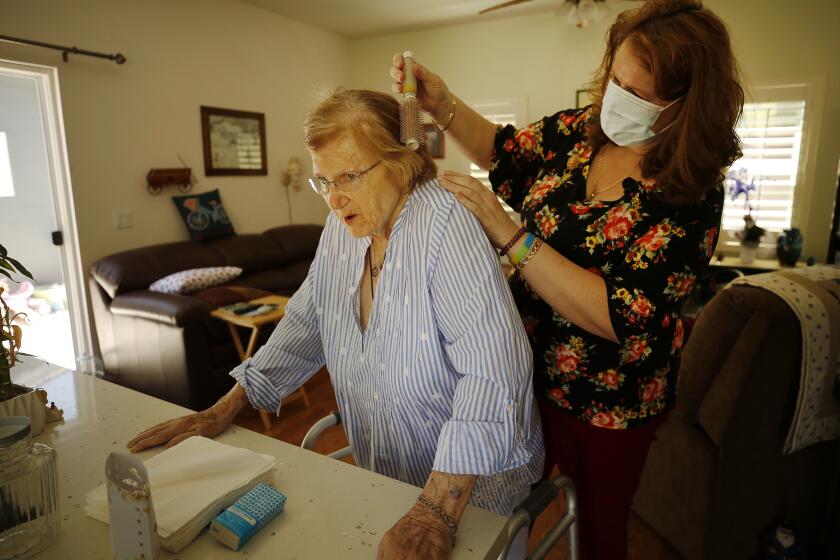 THOUSAND OAKS, CA - APRIL 15: Kim Ballon a Ventura County In Home Support Services (IHSS) care provider attends to Marjorie Williams, 84, at her Thousand Oaks home as California does little to track safety of health care workers during the coronavirus Covid-19 pandemic. Ballon is worried about a lack of protective gear though she regularly cares for elderly clients, helping them bathe and multiple tasks. (keep as a silhouette) Thousand Oaks on Wednesday, April 15, 2020 in Thousand Oaks, CA. (Al Seib / Los Angeles Times)