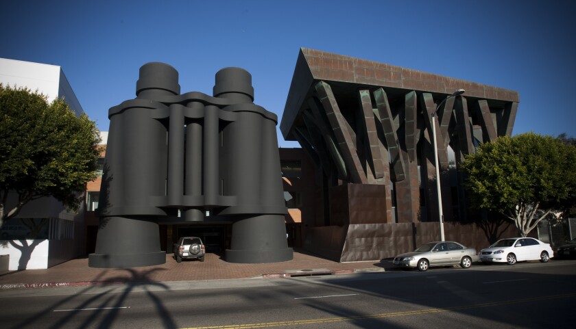 A car drives under what appears to be huge binoculars off a city street.