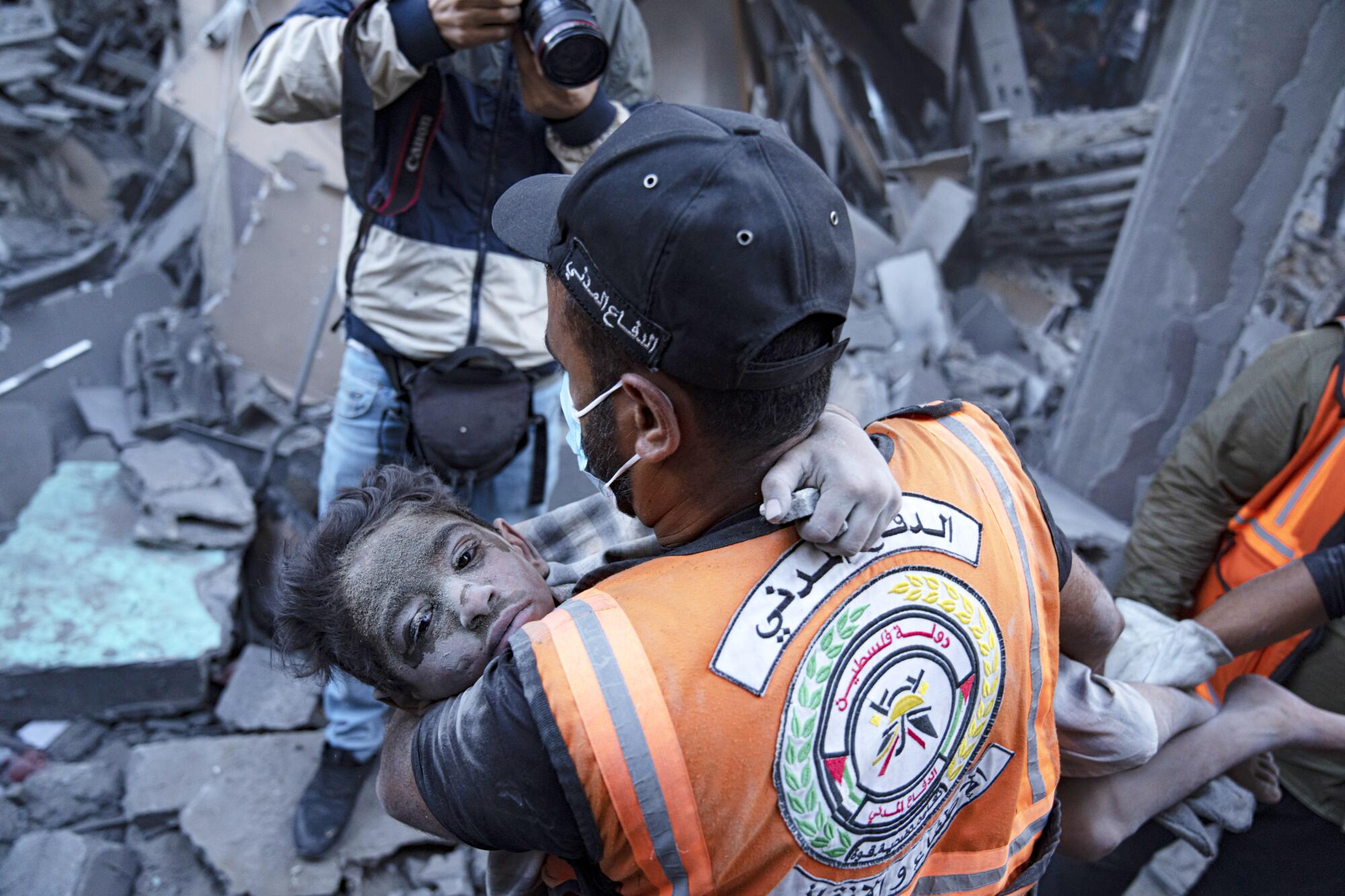 A rescue worker carries a child amid the rubble of a building