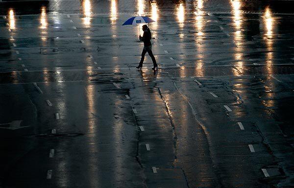A pedestrian totes an umbrella as she makes her way through the rain at Fremont Avenue and 5th Street in downtown Los Angeles.