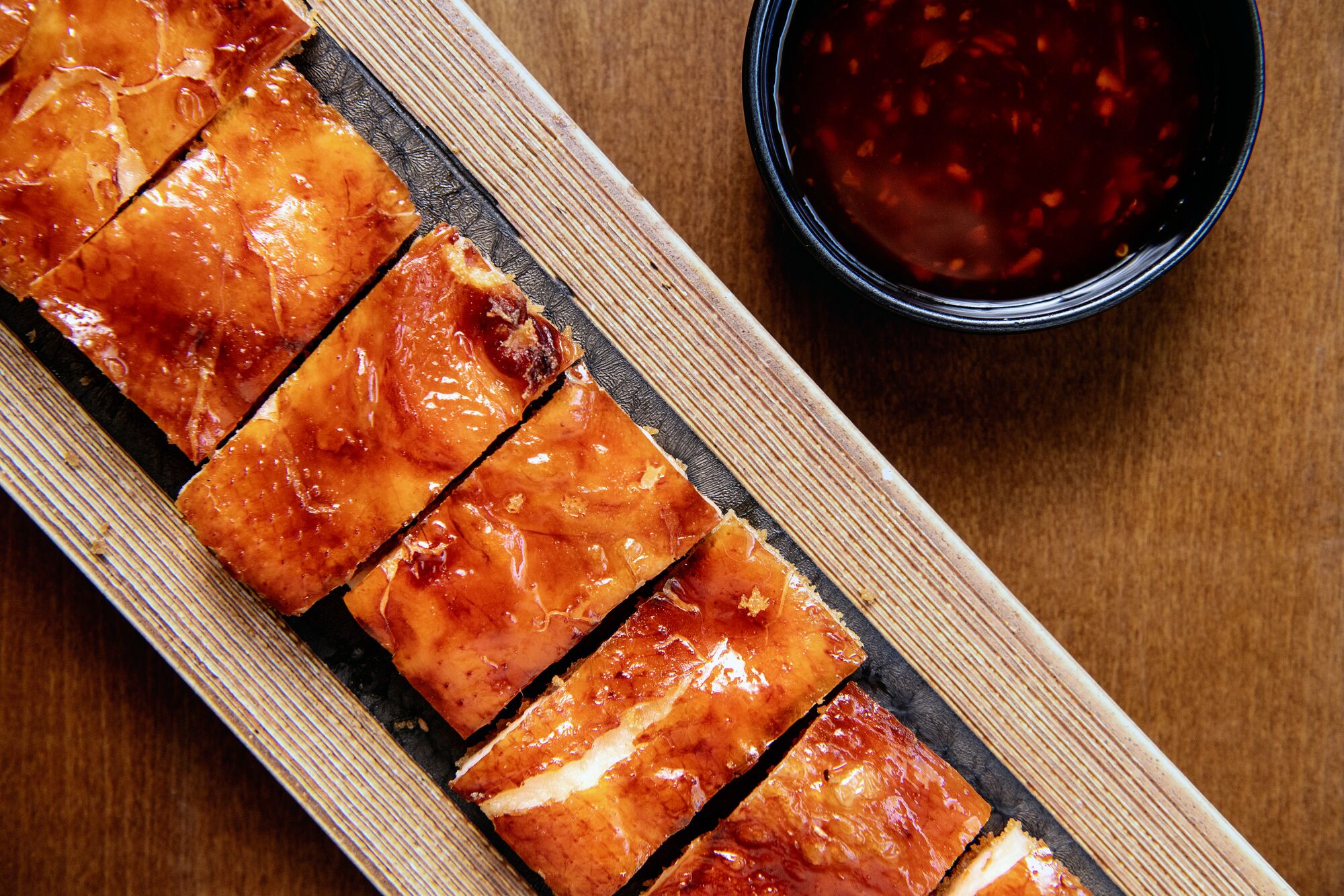 A close up of a vertical place of crispy stuffed chicken, beside a dish of sauce on a brown table.