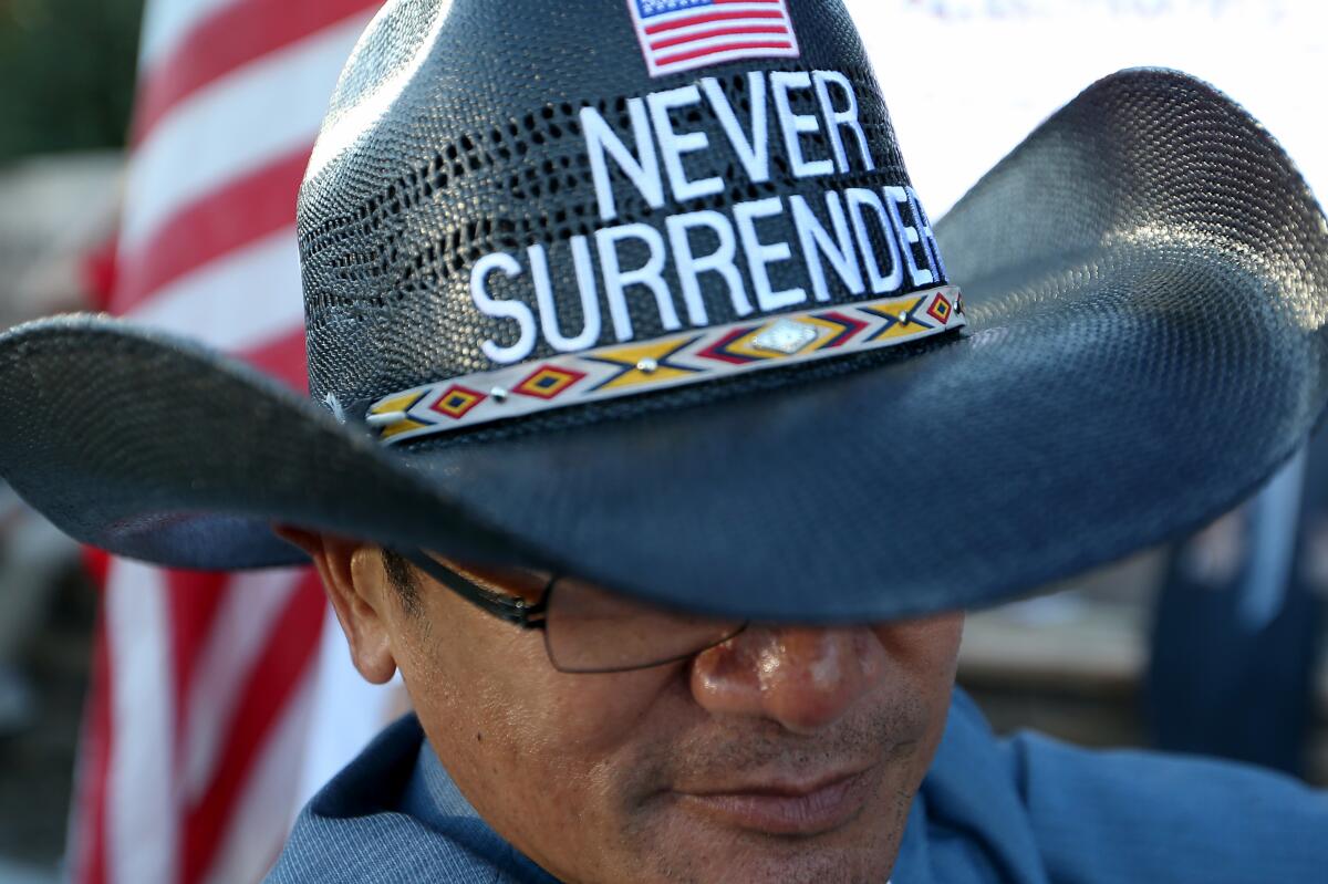A man wears a cowboy hat bearing a U.S. flag and the words 'Never Surrender' 