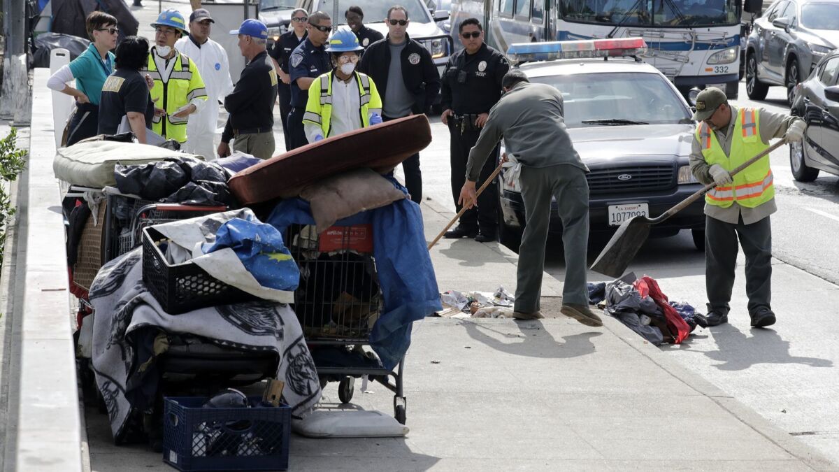 Los Angeles sanitation workers perform a cleanup this month near the new El Puente shelter in the El Pueblo historic district as police escorts watch.