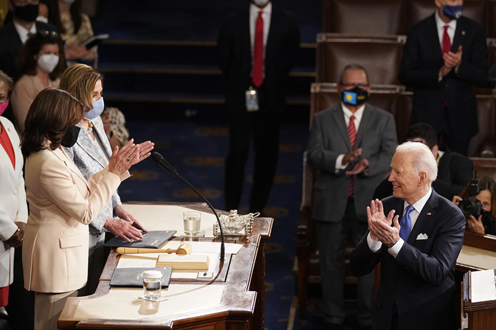 President Biden faces two women on a dais.