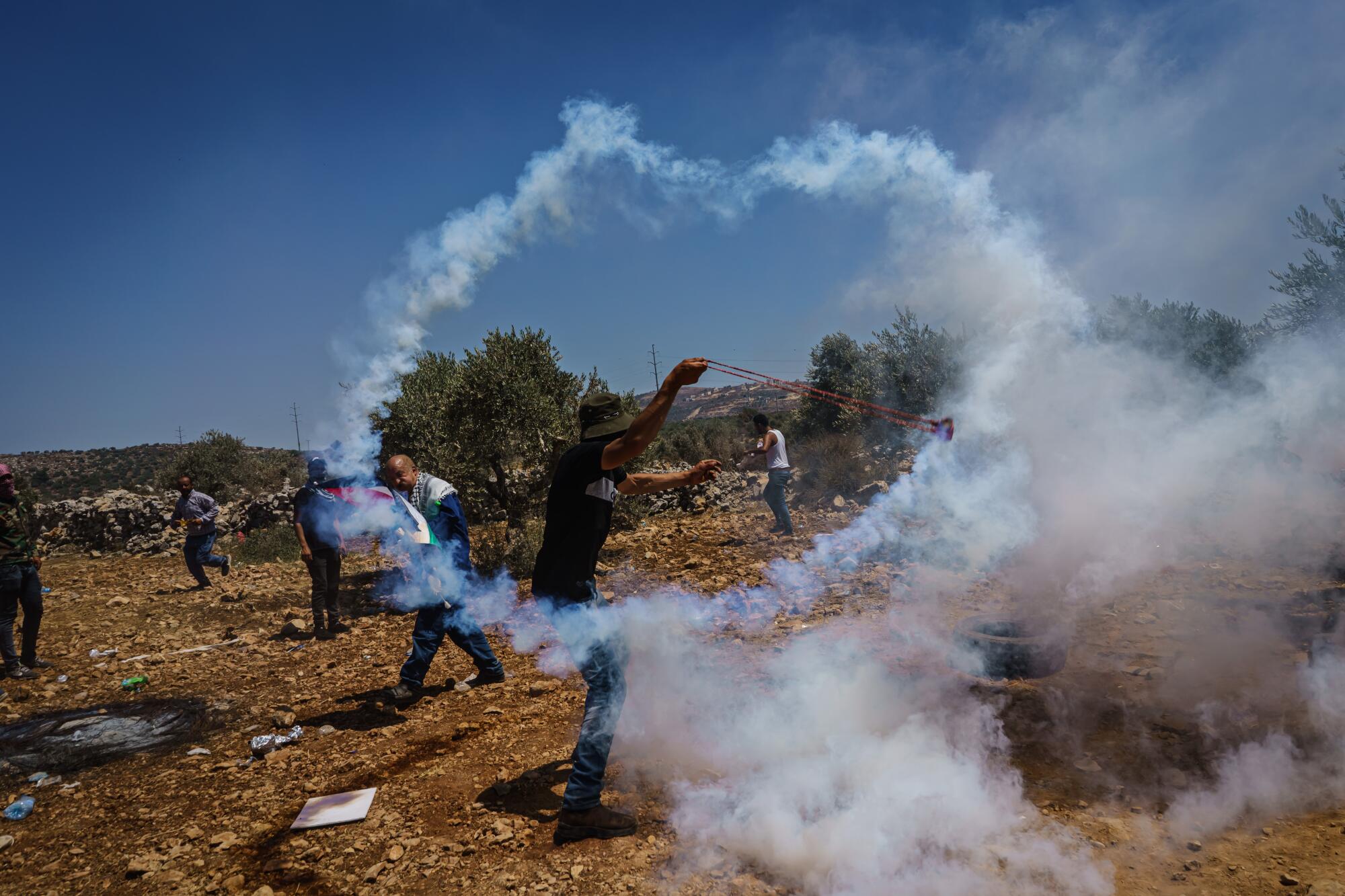 A Palestinians slings a tear gas canister fired by Israeli soldiers as they protest against West Bank Jewish settlement.