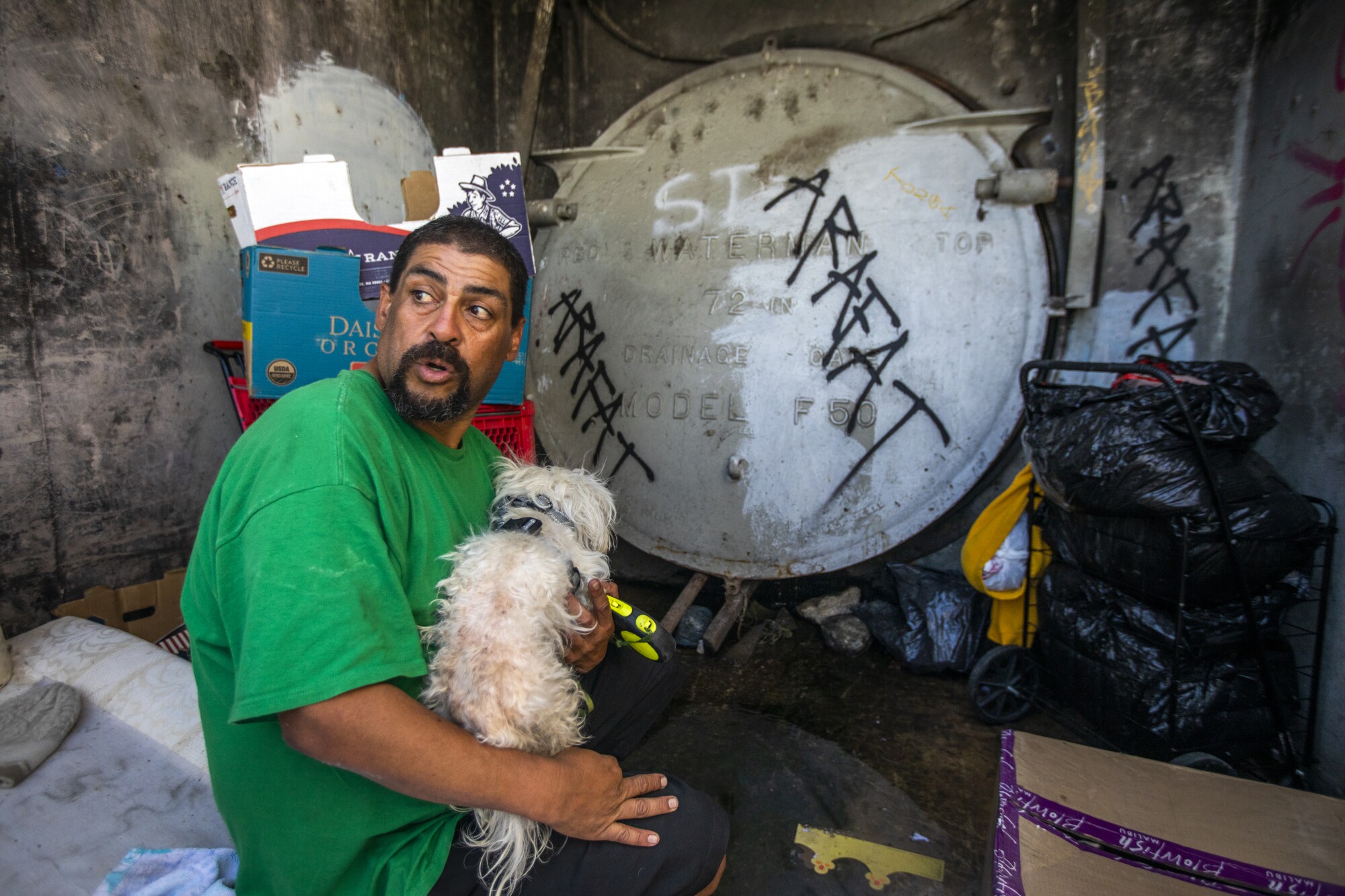A man holds his dog on a broken sofa next to belongings 