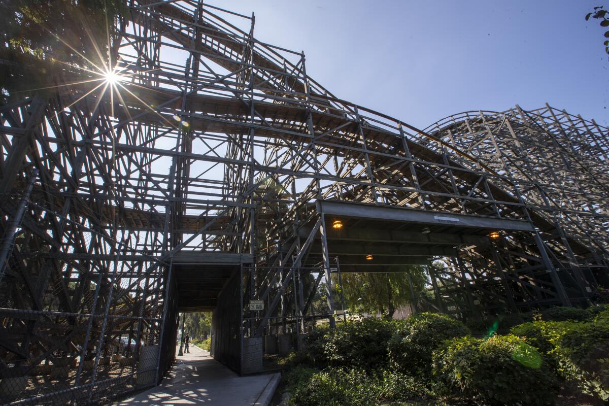 Roller coaster tracks are silhouetted against a blue sky at a theme park.