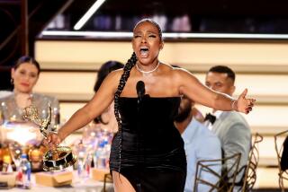 A woman singing onstage with a trophy in her hand and her arms outstretched