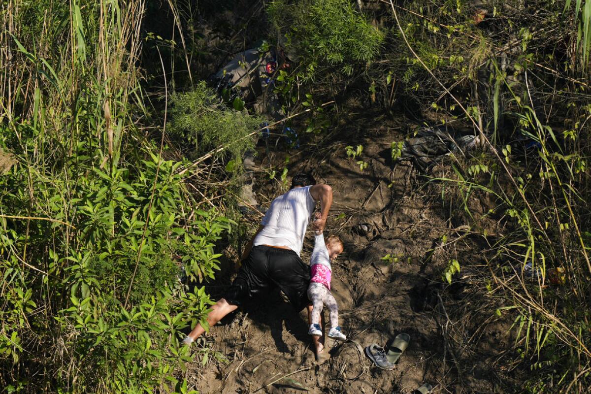 ARCHIVO - Un migrante venezolano sostiene a un niño mientras sube por la orilla de un río