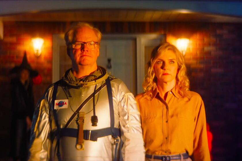 A man in an astronaut suit and a woman stand in front of a house in the movie "Linoleum."
