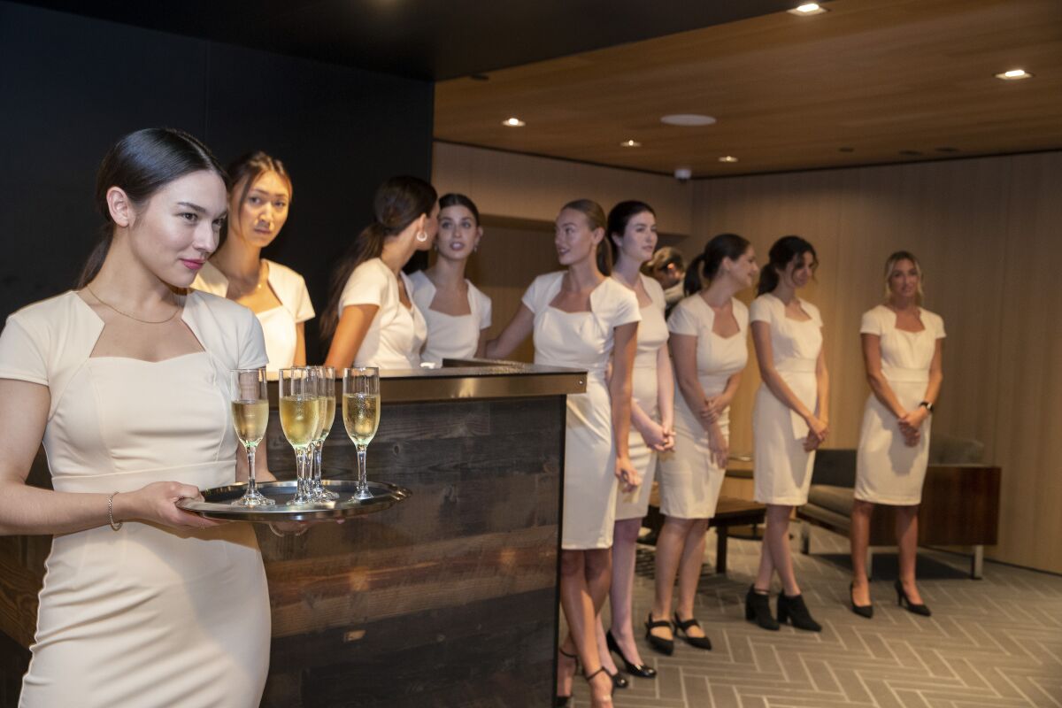 Personal concierges wearing identical cream-colored dresses stand in a line