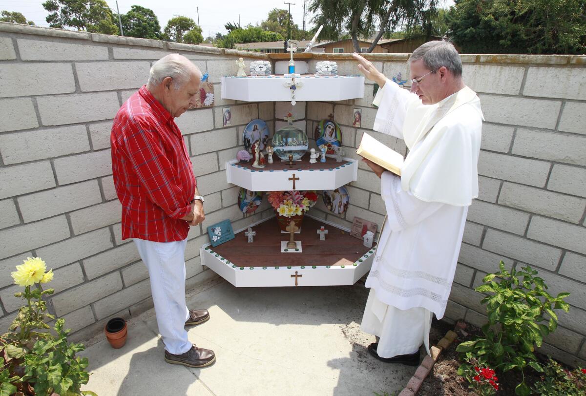 Frank DeSimone, left, listens and prays as Father Augustine Puchner of St. John The Baptist Catholic Church blesses the altar at his home in Costa Mesa on Tuesday.