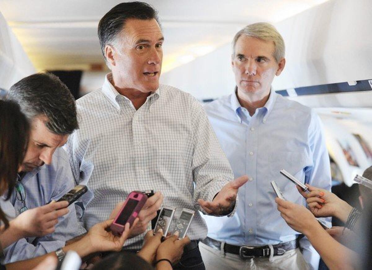 Mitt Romney speaks to reporters aboard his campaign plane as Ohio Senator Rob Portman, right, looks on while in flight to Denver.