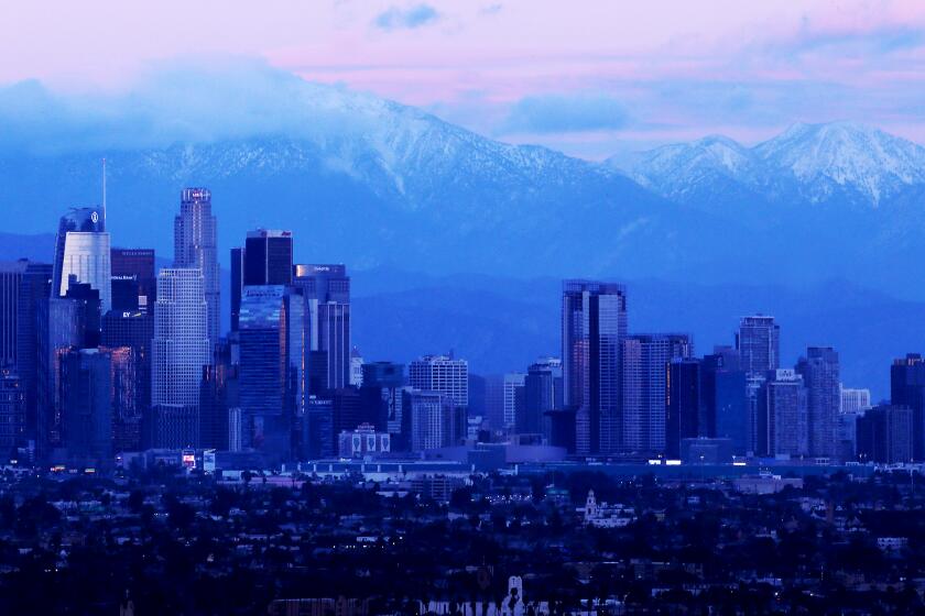 LOS ANGELES, CALIF. - JAN. 1, 2023. The snow-covered Sab Gabriel Mountains provide a dramatic backdrop for the downtown Los Angeles skyline on Jan. 1, 2023. Rain and snow remain in the forecast for Southern California this week. (Luis Sinco / Los Angeles Times)