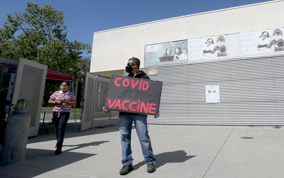 Outreach worker Walter Lopez holds a sign advertising COVID vaccinations at Helen Keller Elementary School in Lynwood.