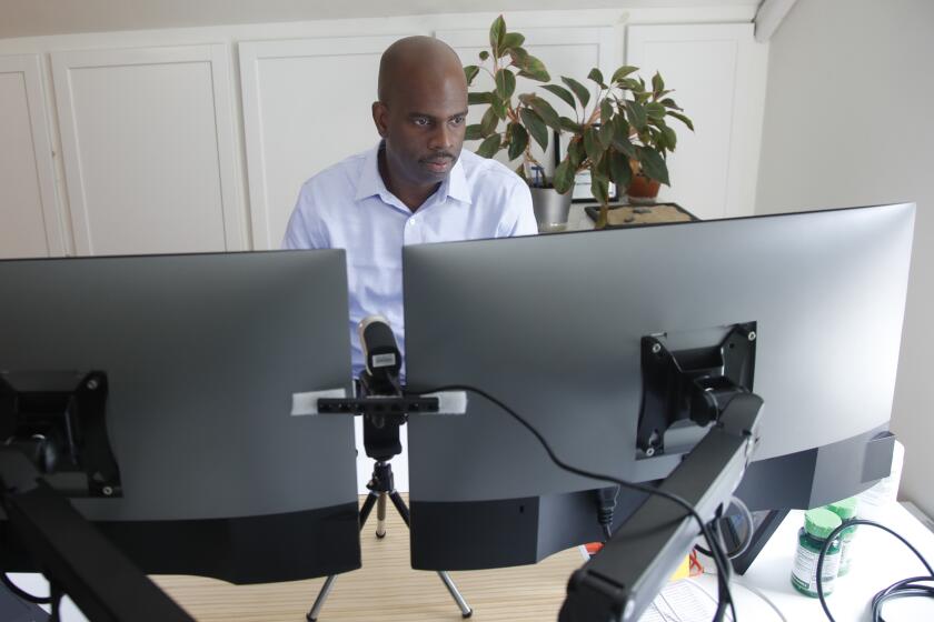 In this June 12, 2020 photo, Gregory Minott works in his home office in Andover, Mass. Minott came to the U.S. from his native Jamaica more than two decades ago on a student visa and was able to carve out a career in architecture thanks to temporary work visas. Now a U.S. citizen and co-founder of a real estate development firm in Boston, he worries that new restrictions on student and work visas expected to be announced soon will prevent others from following a similar path to the American dream. (AP Photo/Elise Amendola)