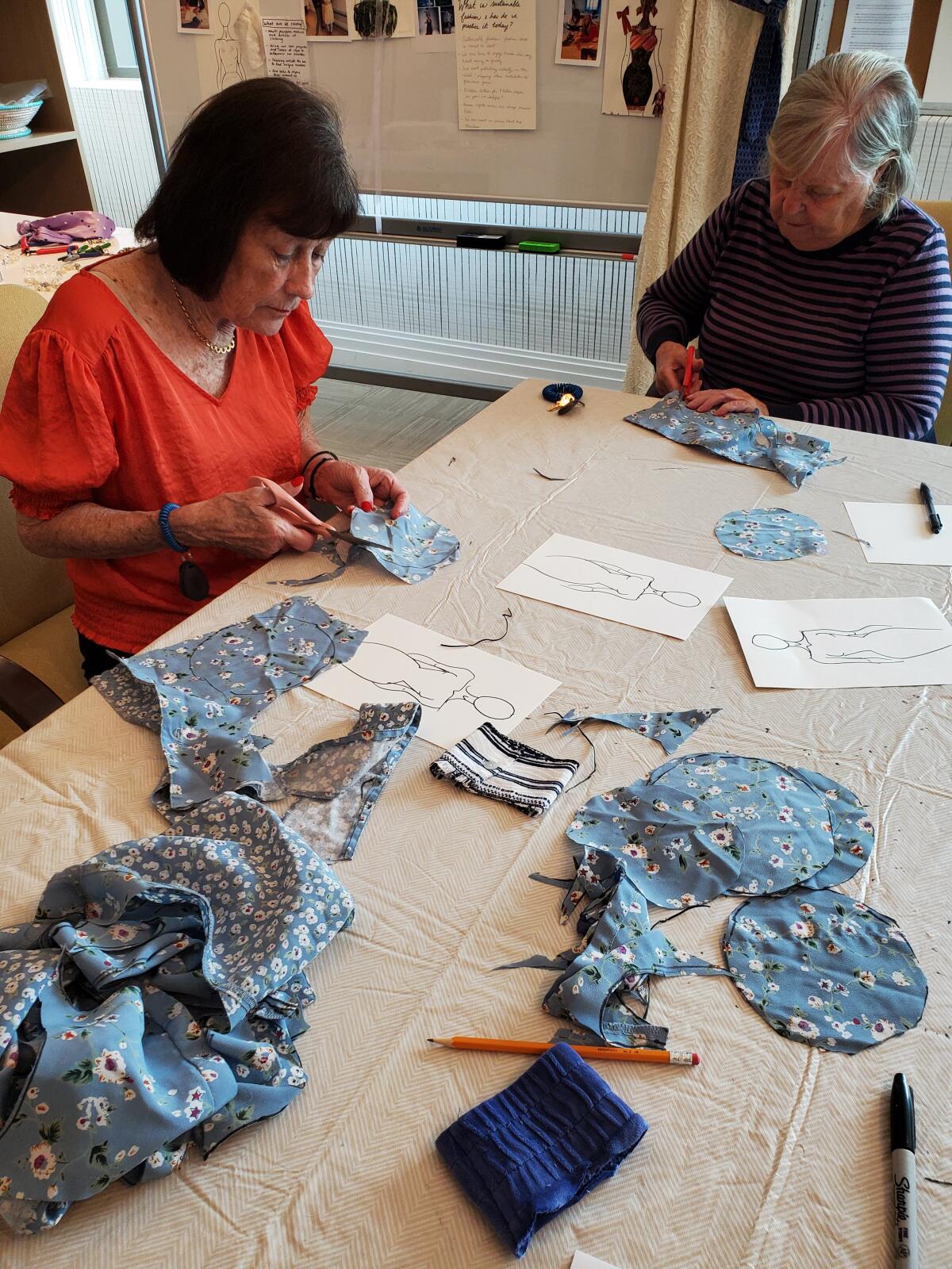 Mornie Wolfson and Jan Canty cut fabric from a shirt into circles that will be made into rosettes and sewn onto a hat.