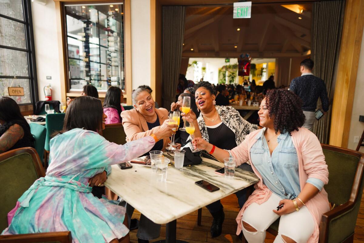 Four women clink glasses in a toast at a white marble table