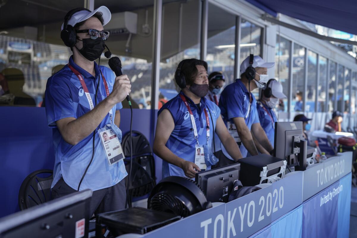 Disc jockey Jeremy Roueche, left, speaks during a men's beach volleyball quarterfinal match at the 2020 Summer Olympics, Thursday, Aug. 5, 2021, Tokyo, Japan. Everyone at the Olympics has had to adjust to the absence of crowds that have stripped the Tokyo Games of their usual flag-waving, anthem-singing spirit. But perhaps no one has faced a bigger challenge than the courtside entertainment at Shiokaze Park. (AP Photo/Petros Giannakouris)