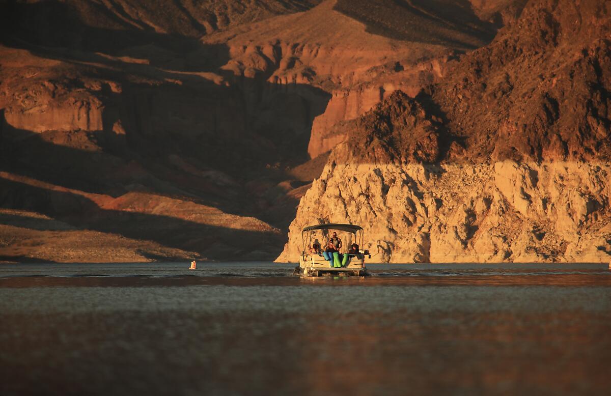 Boaters take a sunset cruise on Lake Mead near rocks with different colored bands.
