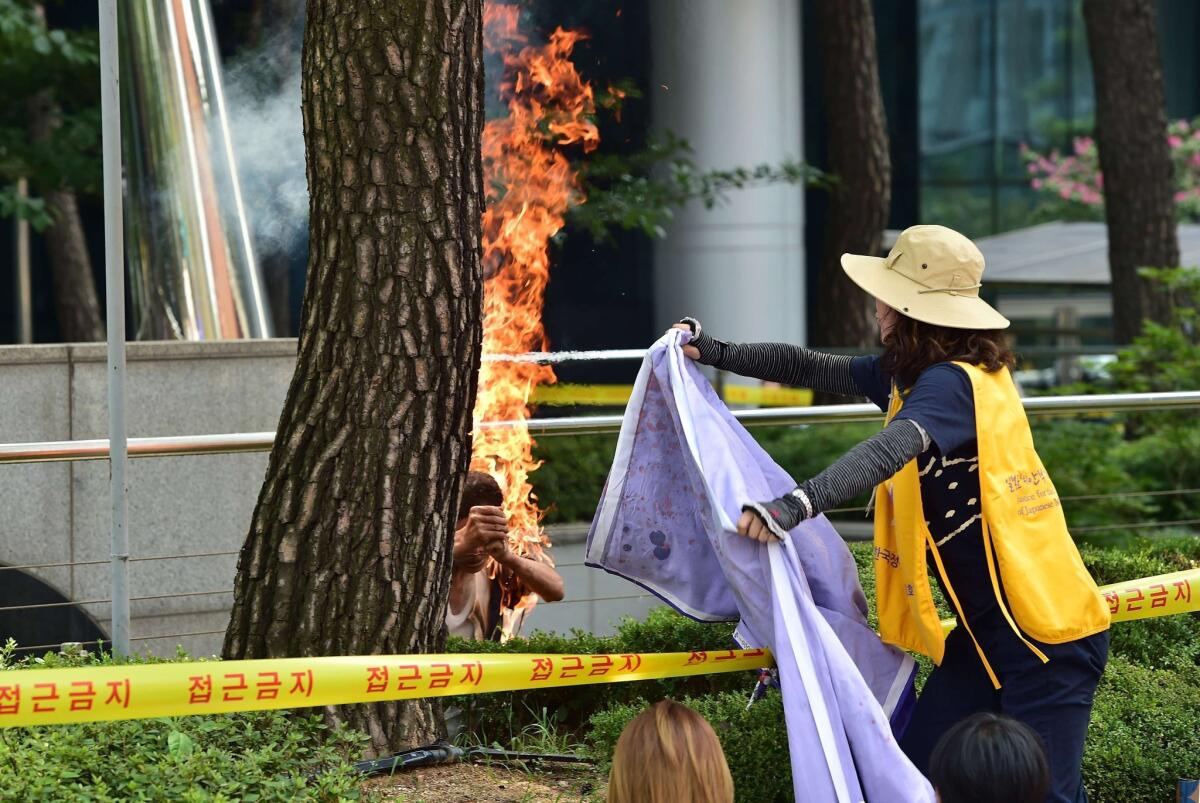 A woman rushes to extinguish the flames after an 81-year-old man set himself on fire in South Korea outside the Japanese embassy during a protest over Japan's wartime conduct.