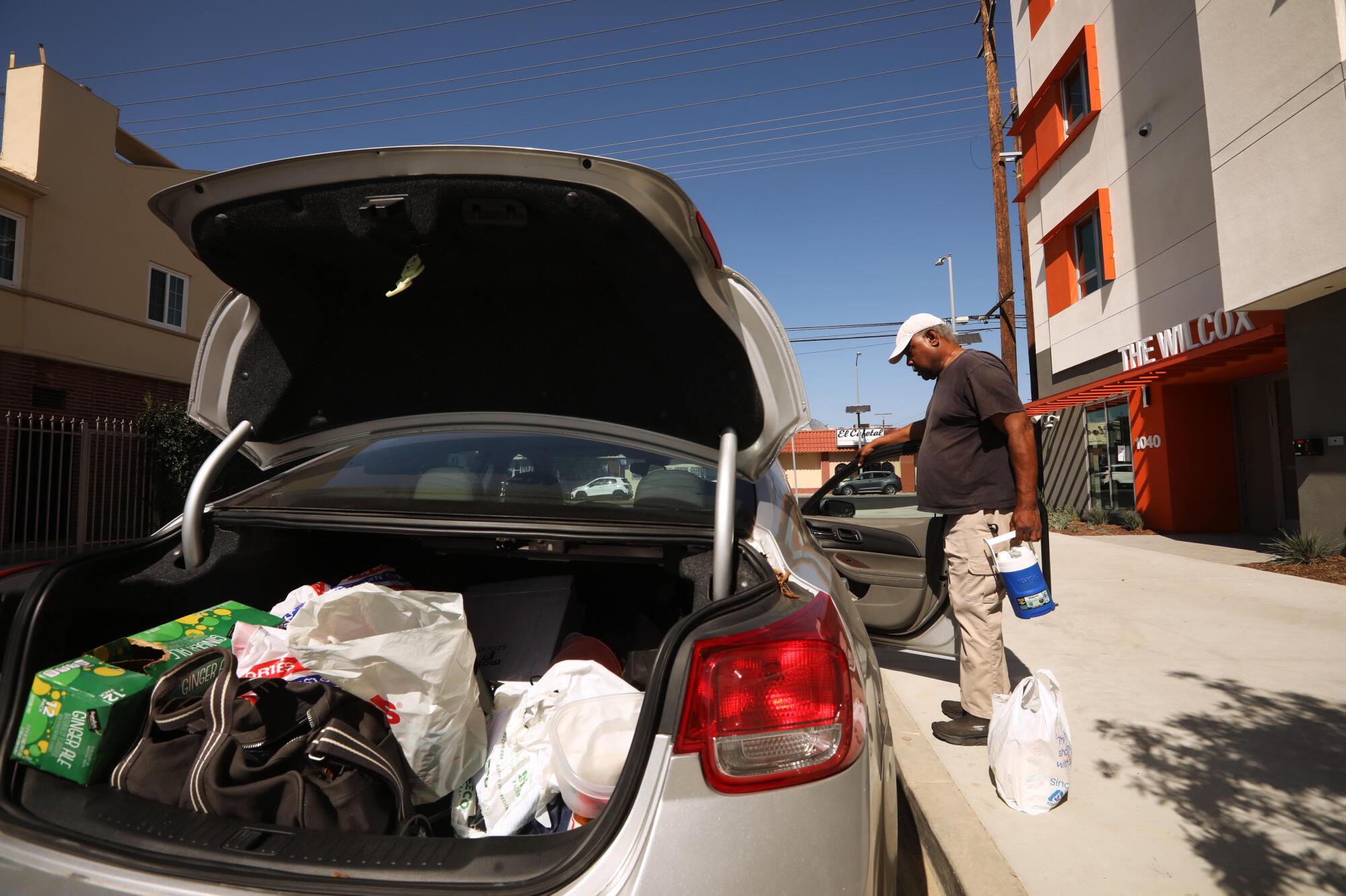 A man moves belongings from the trunk of his car to his new apartment unit.  