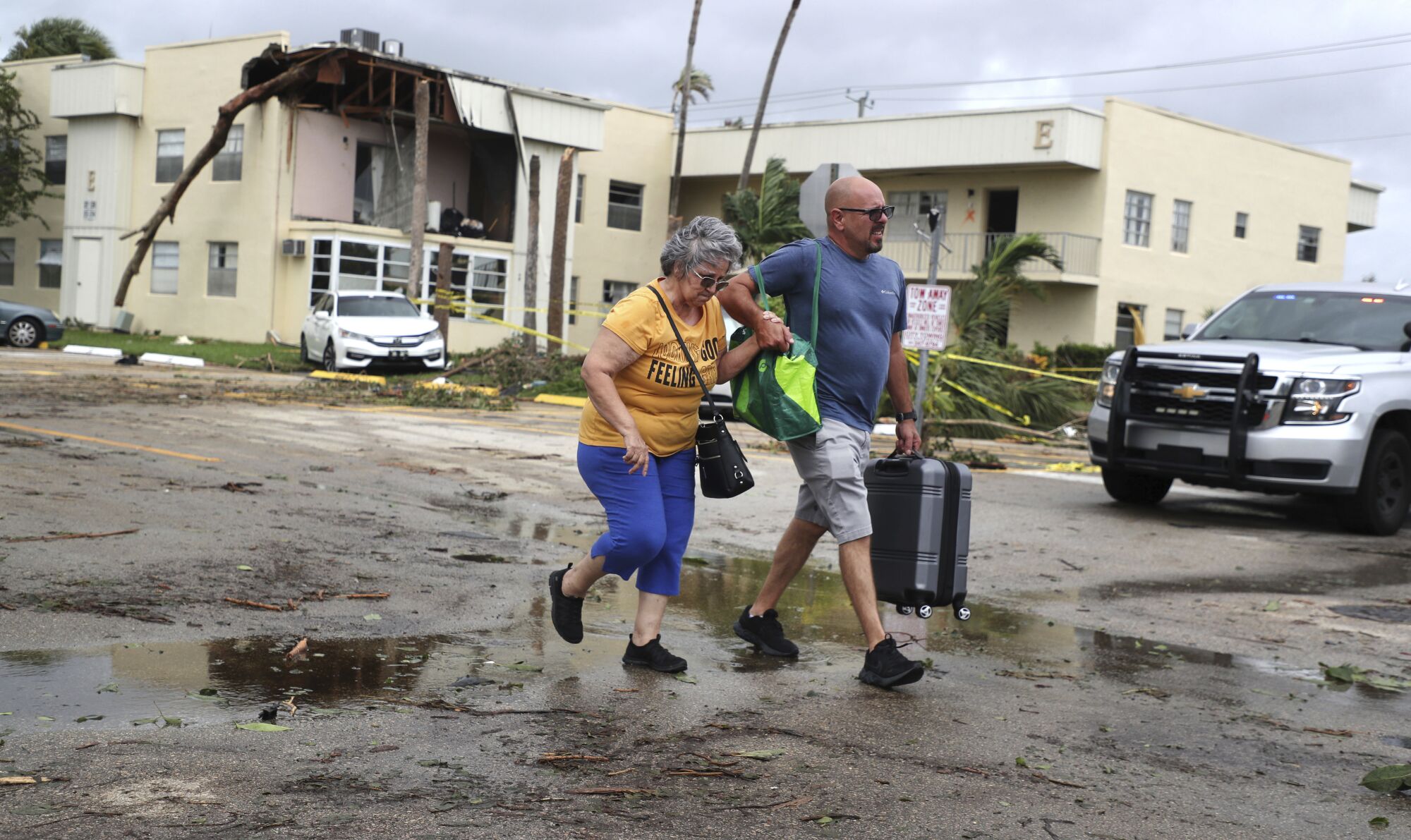 Un homme et une femme traversent le parking d'un immeuble en copropriété endommagé par une tornade apparente