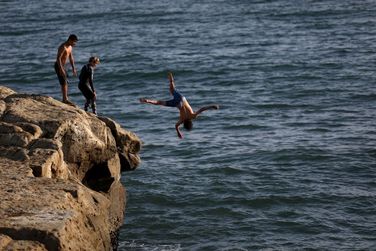 Teenagers jump off a rock into the ocean at Lighthouse Point in Santa Cruz.