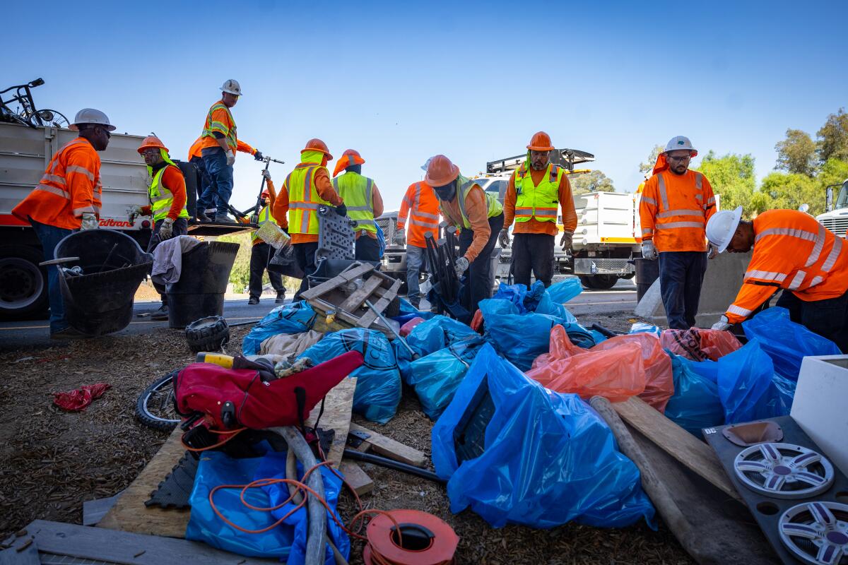 Workers in high-visibility vests and jackets clean up a camp.