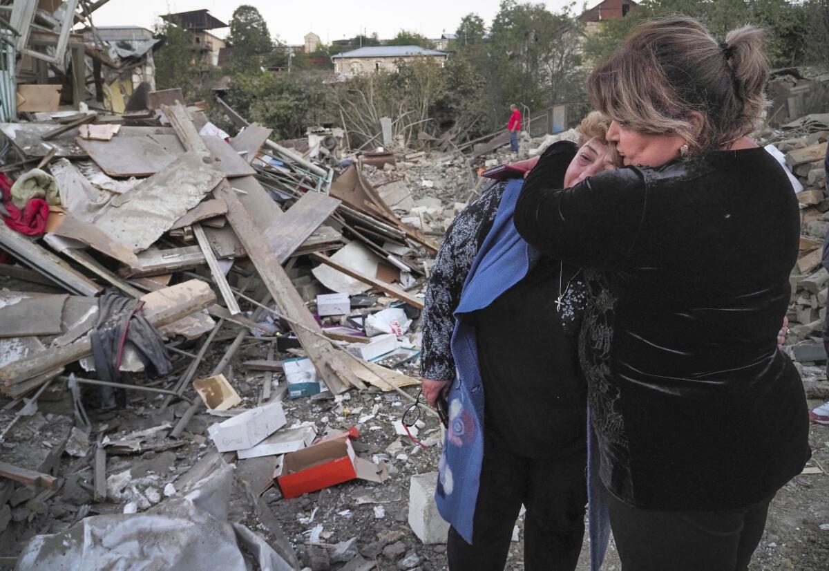 Two women embrace outside the ruins of a home.