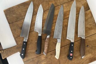 Several different kinds of knives are laid out on a cutting board.