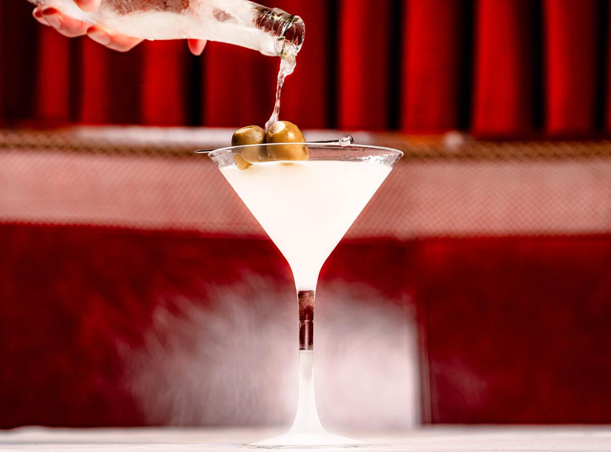 A hand pours a sidecar into "the world's coldest martini" in front of a red leather booth in the new West Hollywood Drake's