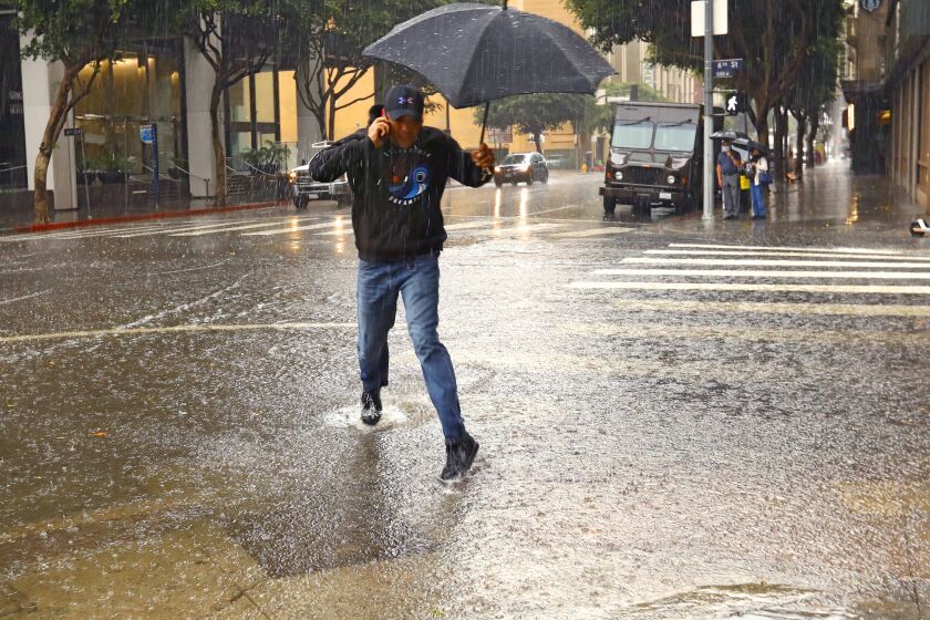 LOS ANGELES CA MARCH 28, 2022 - A man navigates a flooded intersection near Pershing Square in downtown Los Angeles during a downpour Monday morning, March 28, 2022. After a week of generally above-average temperatures, rain fell on much of the Southland. (Carolyn Cole / Los Angeles Times)