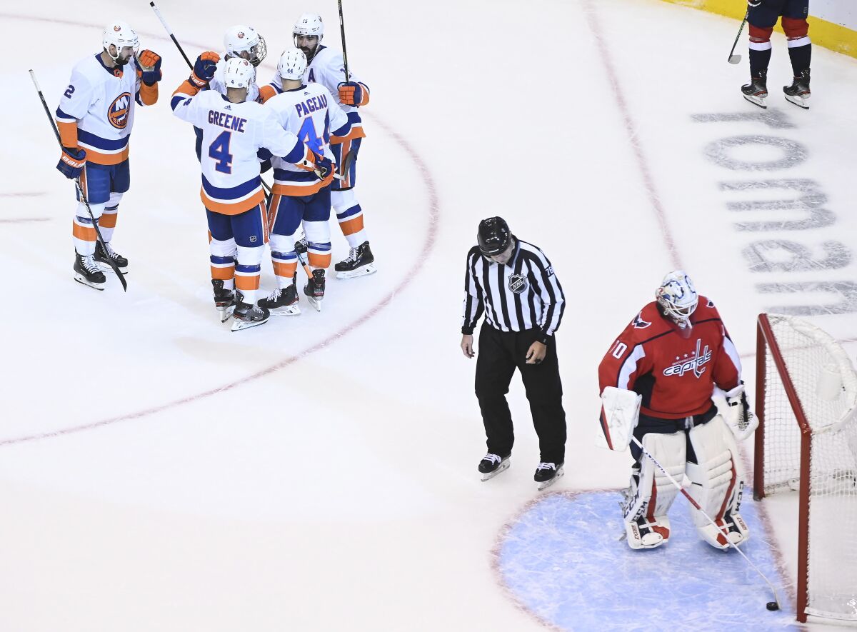 Washington Capitals goaltender Braden Holtby (70) scoops the puck from the net as the New York Islanders celebrate their goal during third-period NHL Eastern Conference Stanley Cup playoff hockey action in Toronto, Friday, Aug. 14, 2020. (Nathan Denette/The Canadian Press via AP)