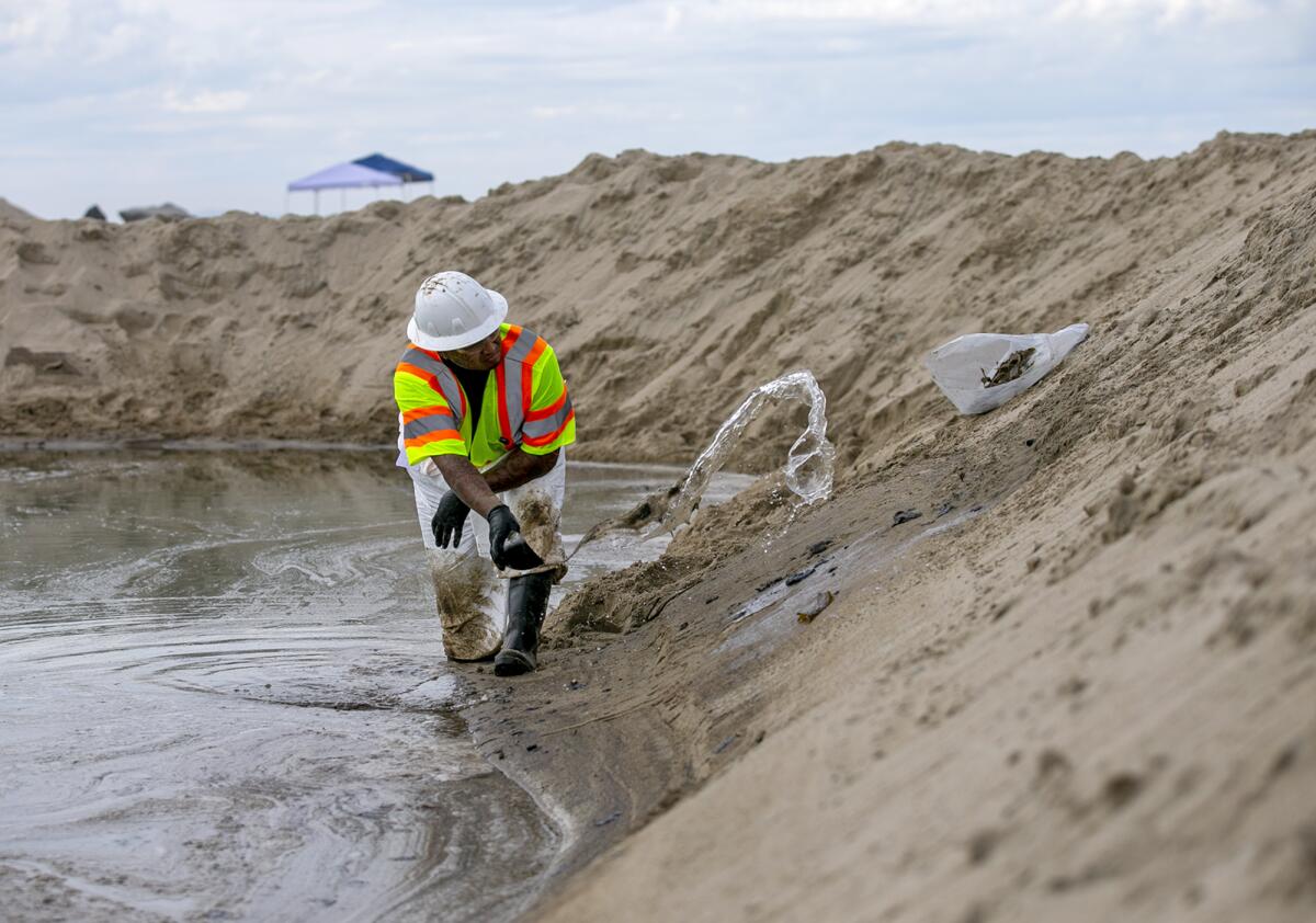 An employee with West Coast Environmental Solutions scoops oil out of a pool of water at the mouth of the Santa Ana River.