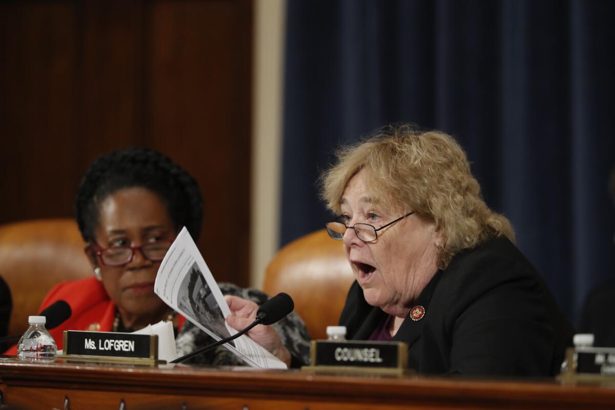 A woman leans forward as she speaks into a microphone. To her left, another woman listens.