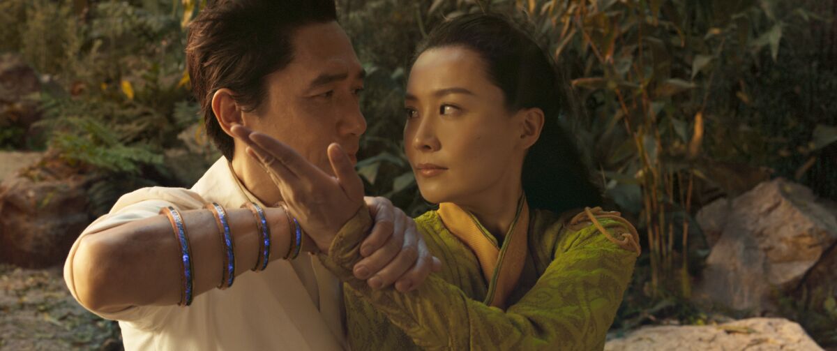 A man wearing armbands on his forearm holds a woman's wrist as they lock eyes up close in a scene from "Shang-Chi"