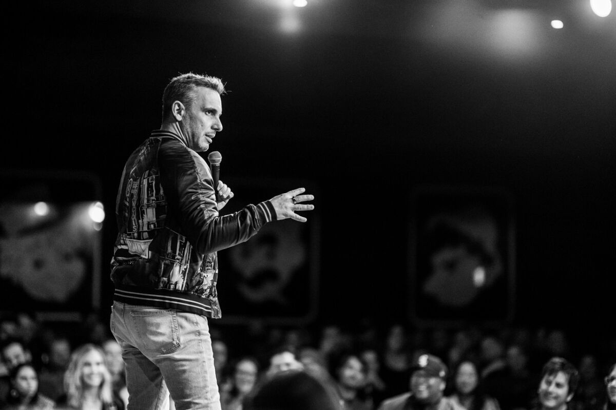 A black and white photo of a man in a bomber jacket doing standup