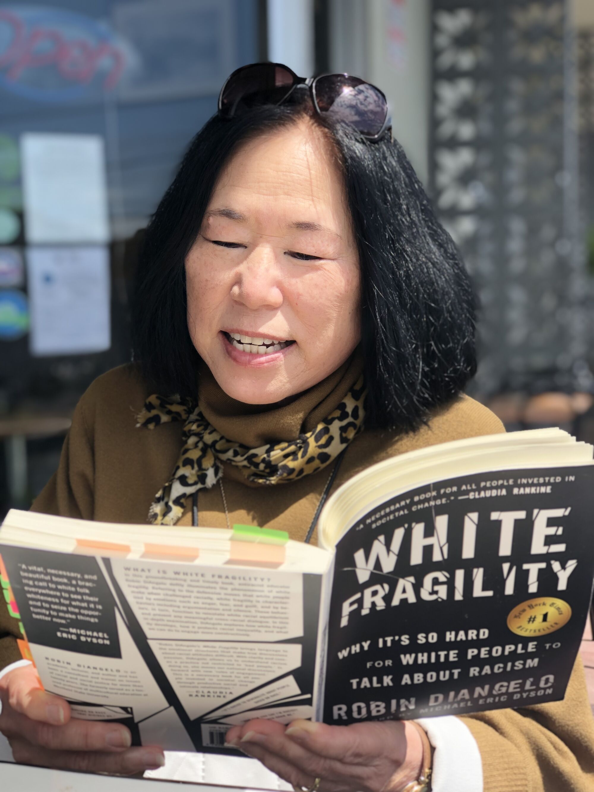 A woman reading aloud from a paperback copy of "White Fragility" by Robin DiAngelo.