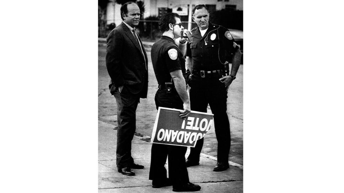 A police officer holds part of a sign seized at a polling place in Santa Ana in 1988, when uniformed guards were stationed at 20 polling sites in the city by the GOP.
