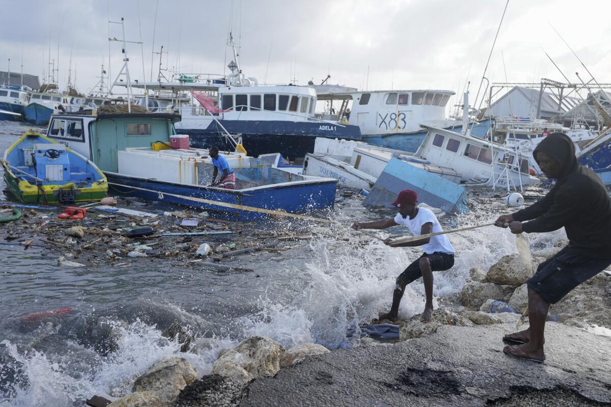 Two men hold a rope on a dock next to damaged boats.