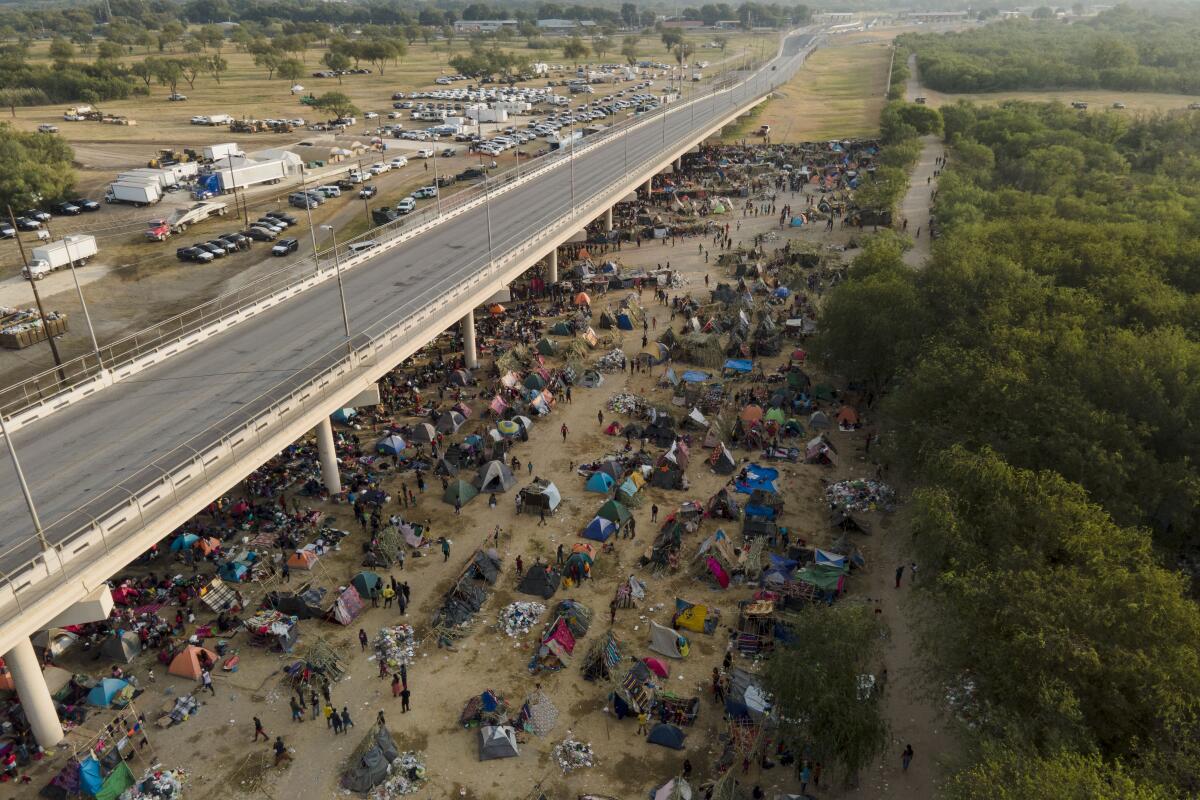 A throng of migrants camped under and beside a roadway bridge. 