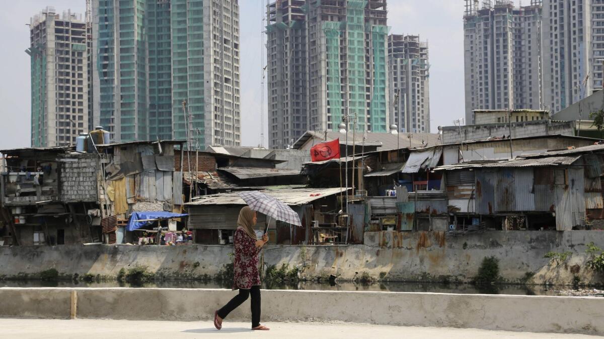 A woman walks along a city canal as new office and apartment buildings rise over a slum in Jakarta, Indonesia, in 2014.