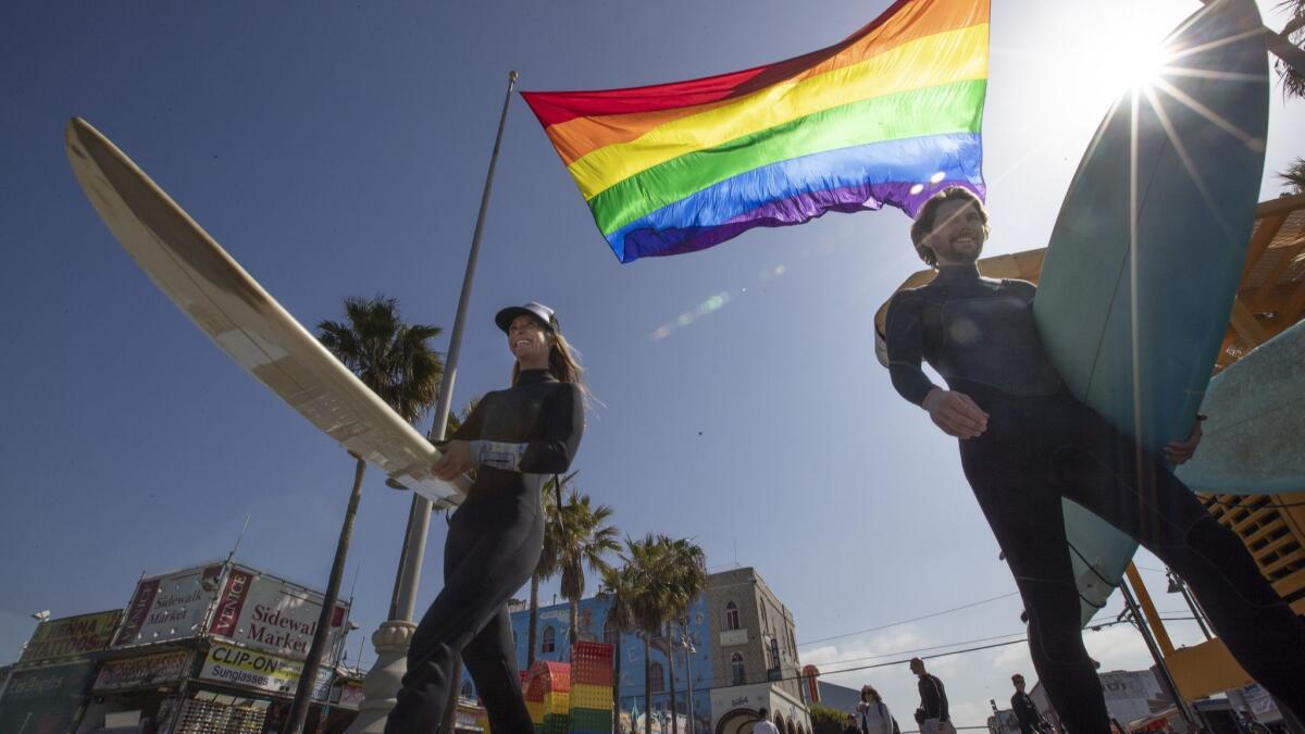 Surfers head for the waves beneath a giant rainbow flag made by Gilbert Baker that was unveiled in Venice on June 1, 2018.