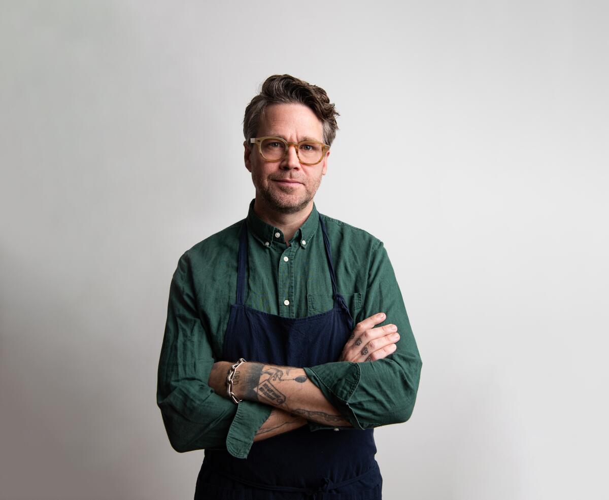 Chef Marcus Jernmark stands in a collared shirt and an apron, arms crossed and looking at camera