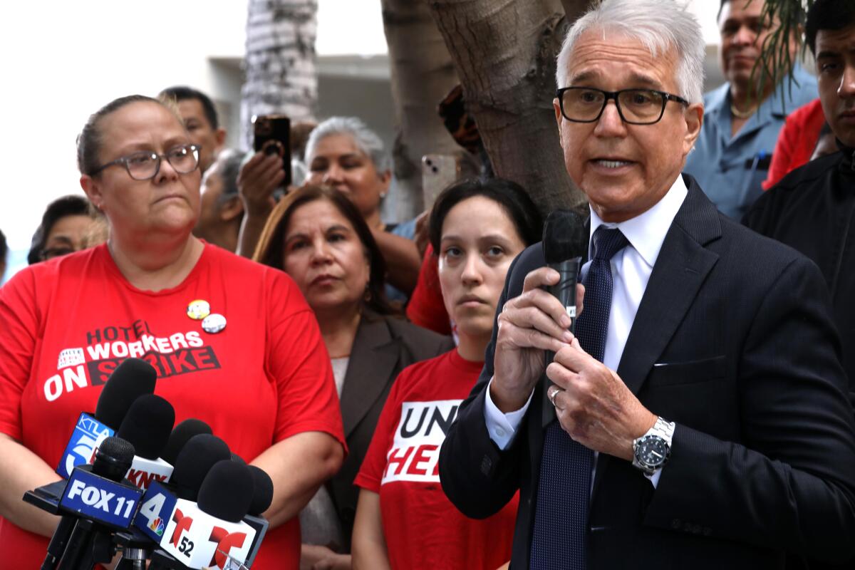 a man in a suit with white hair speaks as he is surrounded by people in red T shirts